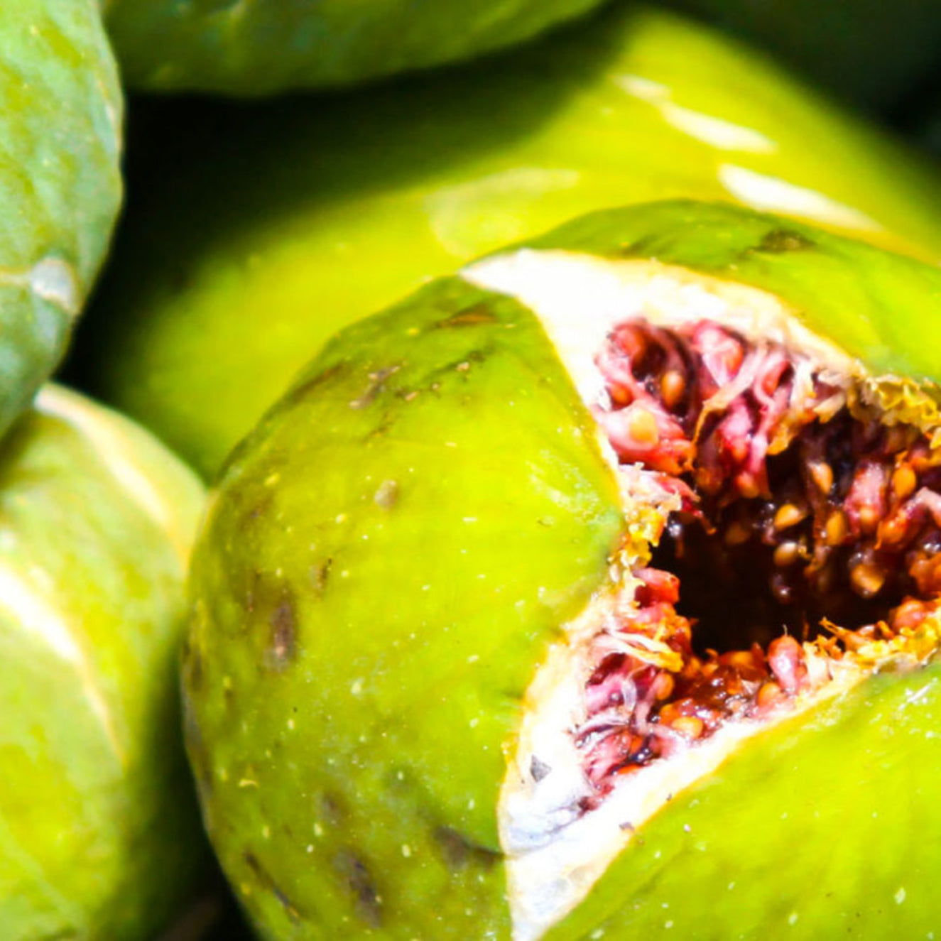 Close-up of green figs with one cut open to reveal its interior.