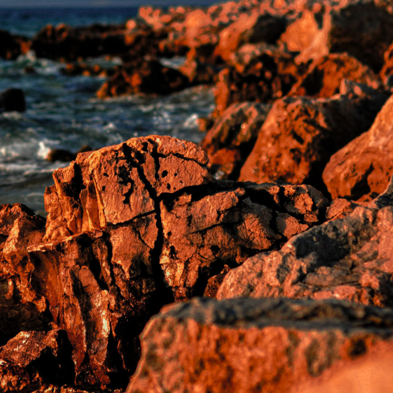 Close-up of red-orange rocks with ocean waves in the background